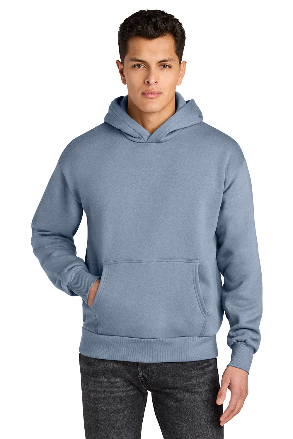 A man wearing a dusty blue pullover hoodie with a front kangaroo pocket, paired with dark gray jeans, photographed against a solid white background. Next Level Apparel® Heavyweight Hoodie, Embroidered