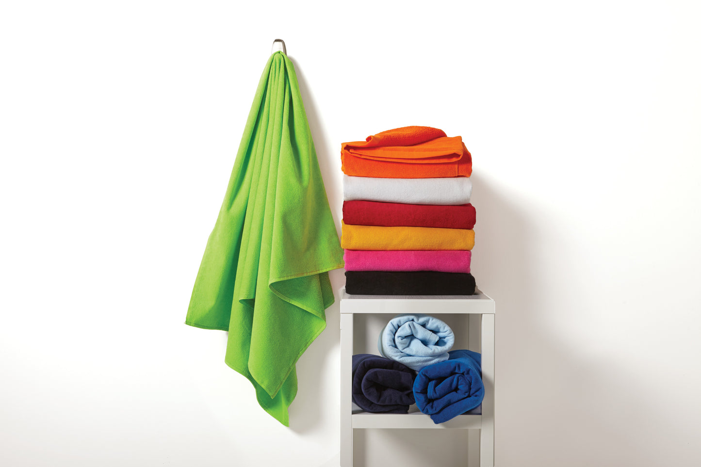 Colorful towels on a white shelf against a white background. Port Authority® Cabana Beach Towel, Embroidered by Helmsman Stitch Co.