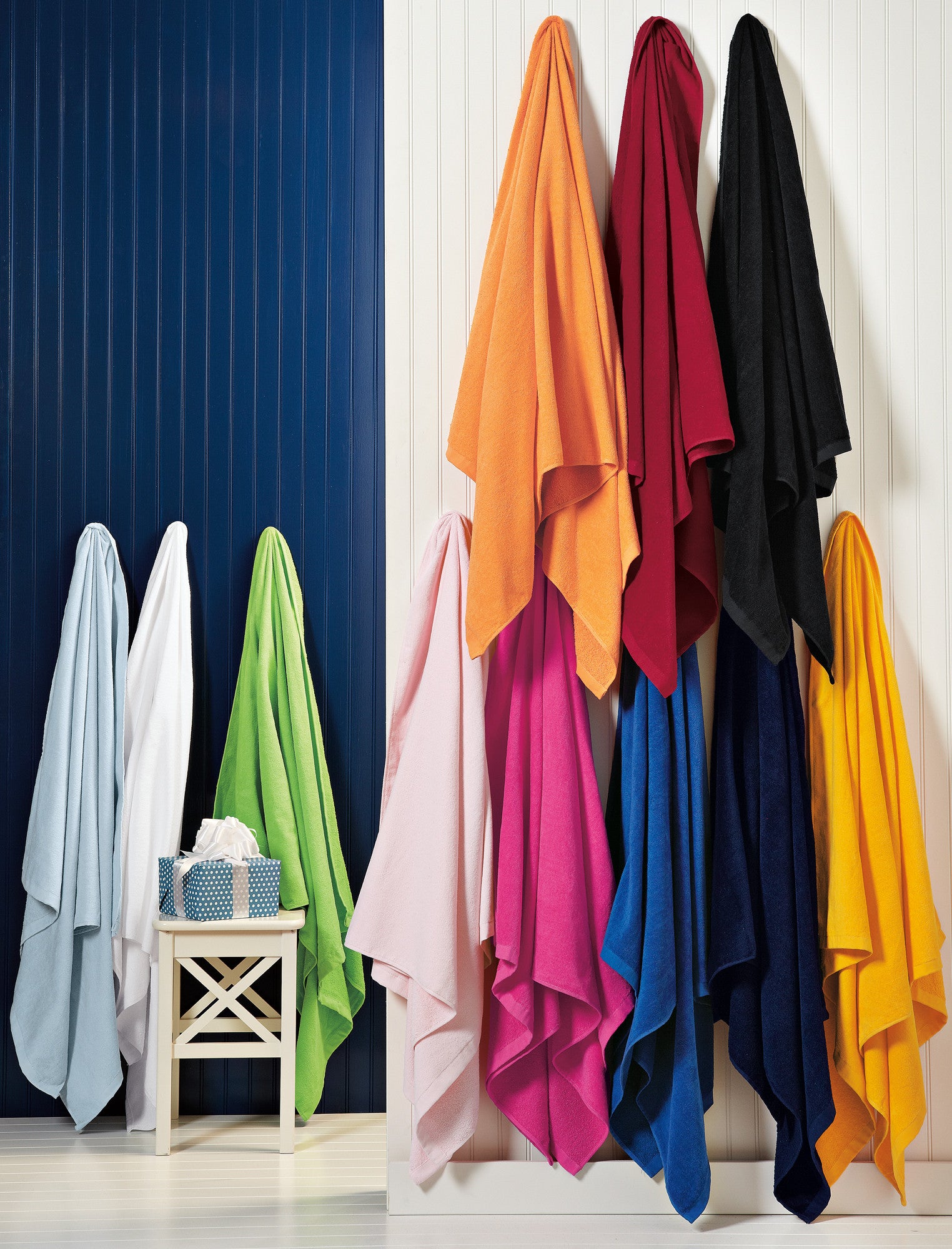 Colorful towels hanging on a rack against a white wall. Port Authority® Cabana Beach Towel, Embroidered by Helmsman Stitch Co.