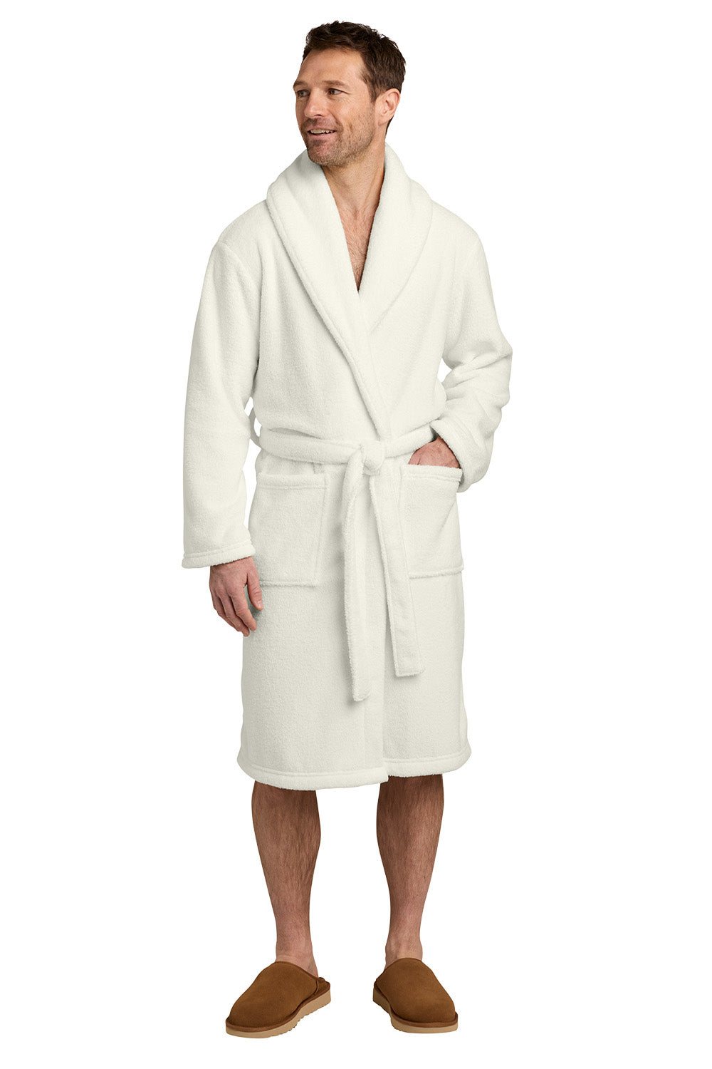 A man wearing a plush white bathrobe with a shawl collar, front patch pockets, and a matching tie belt, standing against a plain white background. He is wearing brown slippers. Port Authority® Dream Plush Robe, Embroidered