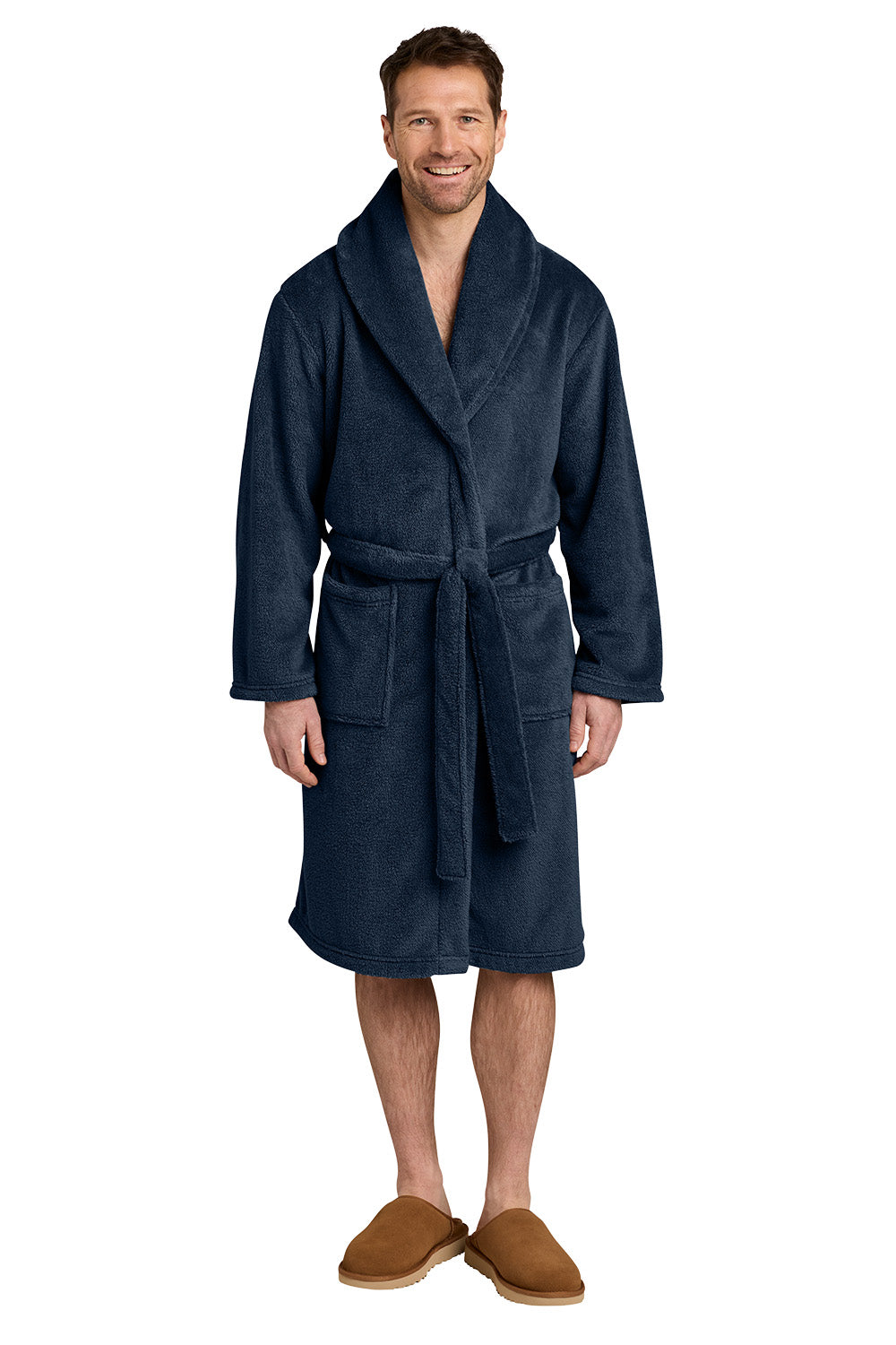 A man wearing a dark navy blue plush bathrobe with a matching tie belt, paired with brown slippers, standing against a plain white background. Port Authority® Dream Plush Robe, Embroidered