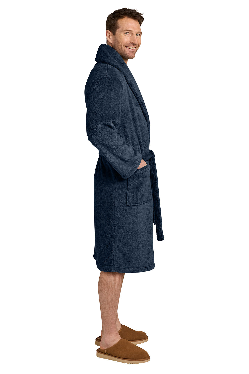 A man wearing a dark navy blue plush bathrobe and brown slippers, standing in profile against a solid white background. Port Authority® Dream Plush Robe, Embroidered