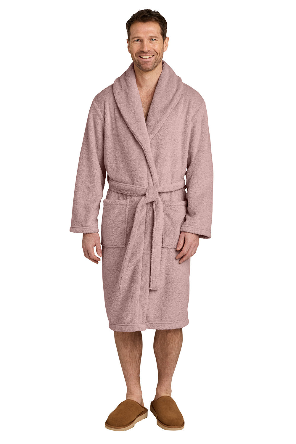A smiling man wearing a dusty pink plush bathrobe with a shawl collar and tie belt, paired with brown slippers, against a plain white background. Port Authority® Dream Plush Robe, Embroidered