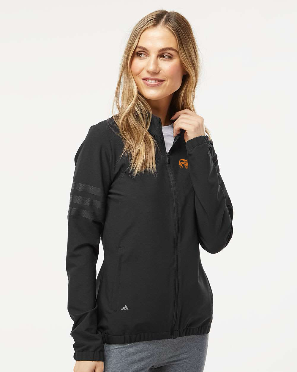 Woman wearing a black Adidas jacket on a white background. Adidas Women's Wind Resistant Full-Zip Jacket, RAM Logo by Helmsman Stitch Co. 
