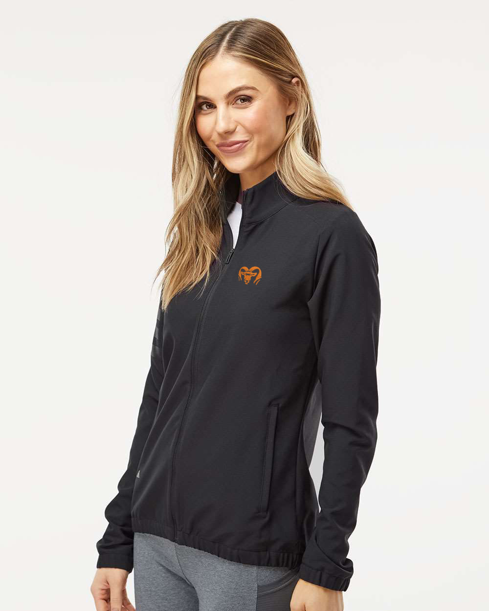 Woman wearing a black jacket with a brand logo on a white background. Adidas Women's Wind Resistant Full-Zip Jacket, RAM Logo by Helmsman Stitch Co. 