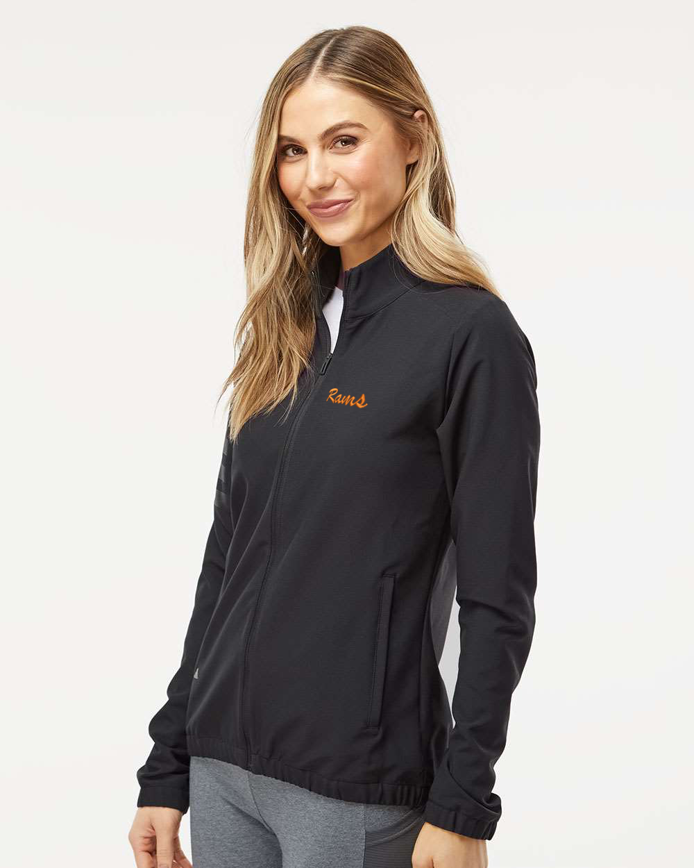 Woman wearing a black jacket with a brand logo on a white background. Adidas Women's Wind Resistant Full-Zip Jacket, RAM Logo by Helmsman Stitch Co. 