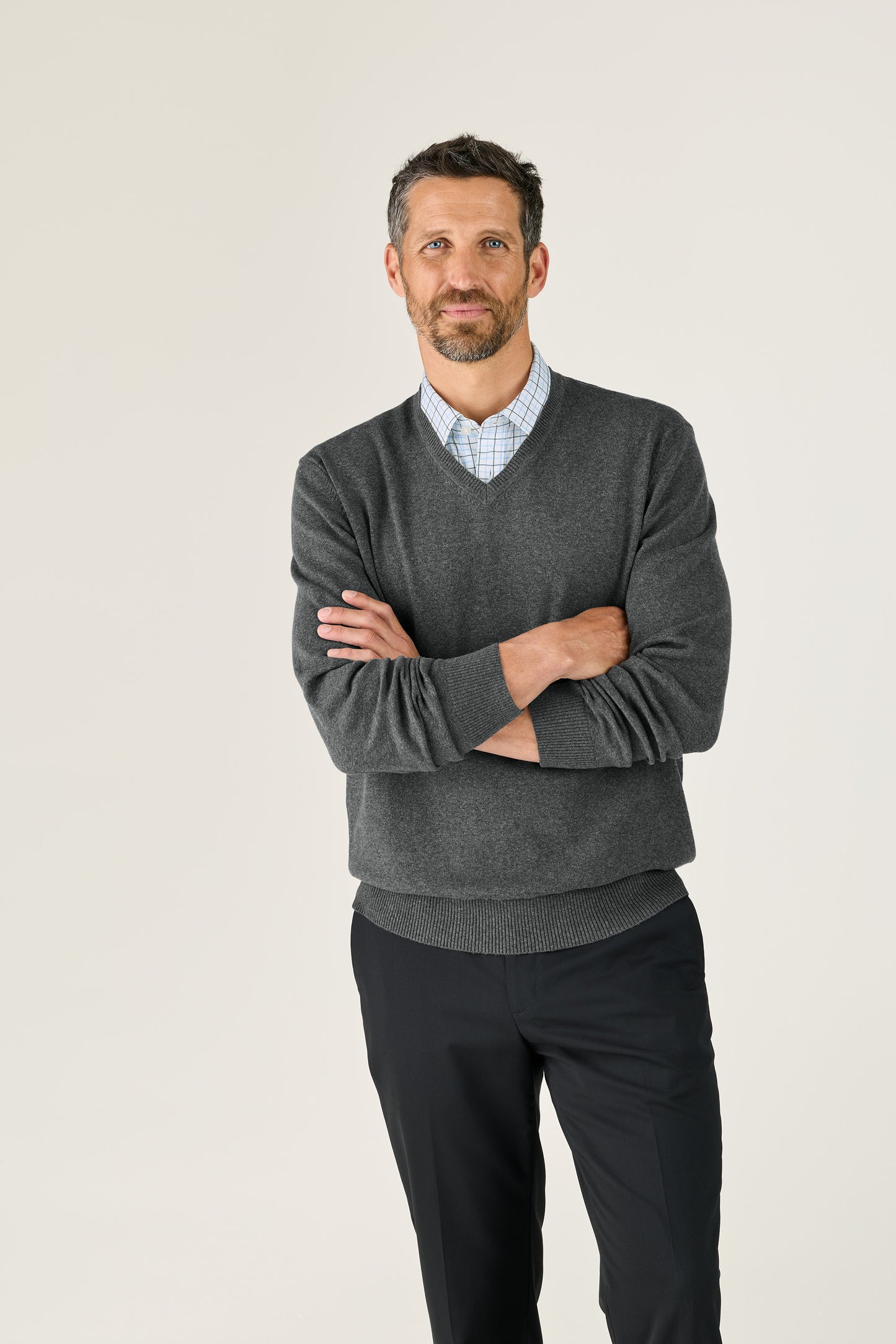 Man wearing a gray sweater over a checkered shirt with black pants on a white background. Port Authority® Easy Care V-Neck Sweater, Embroidered
