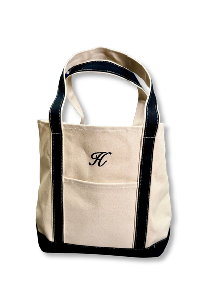 Custom Tote, Superior MI Tote, XL, Open Top, Helmsman Stitch Company. A cream canvas tote bag with black trim and dual shoulder straps, featuring a front pocket with an embroidered black monogram letter 'H' on the front, set against a plain white background. Makes great gifts.
