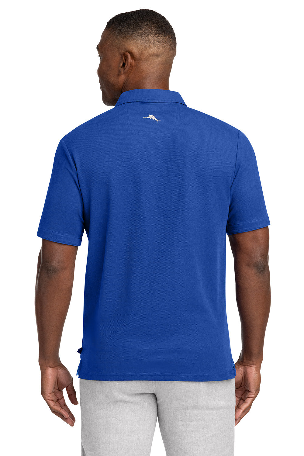 Man wearing a blue polo shirt with a logo on the back, standing against a white background Tommy Bahama® 5 O’Clock Polo, Embroidered
