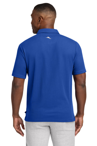 Man wearing a blue polo shirt with a logo on the back, standing against a white background Tommy Bahama® 5 O’Clock Polo, Embroidered
