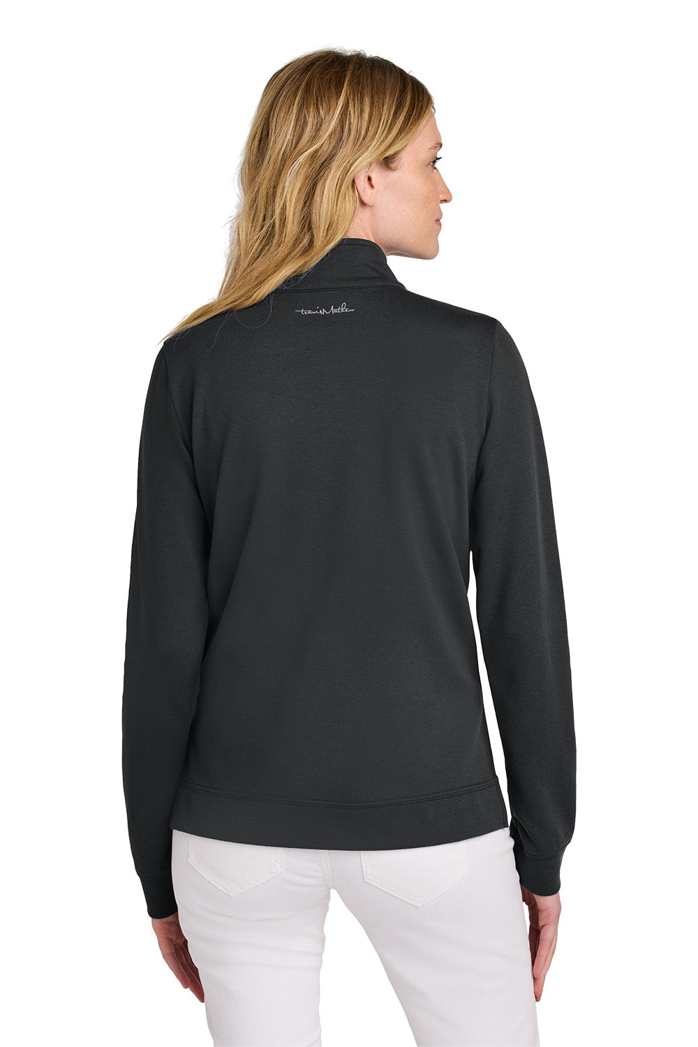 Woman wearing a black jacket with a visible brand logo on the back, standing against a white background. TravisMathew Women's Coveside 1/2-Zip, Embroidered