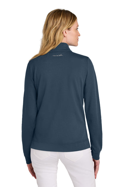 Woman wearing a navy blue jacket with a visible brand logo on the back, standing against a white background. TravisMathew Women's Coveside 1/2-Zip, Embroidered