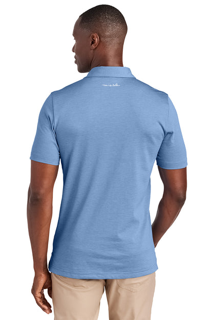 Man wearing a blue polo shirt with a visible brand logo on the back, standing against a white background. Embroidered TravisMathew Sunnyvale Polo