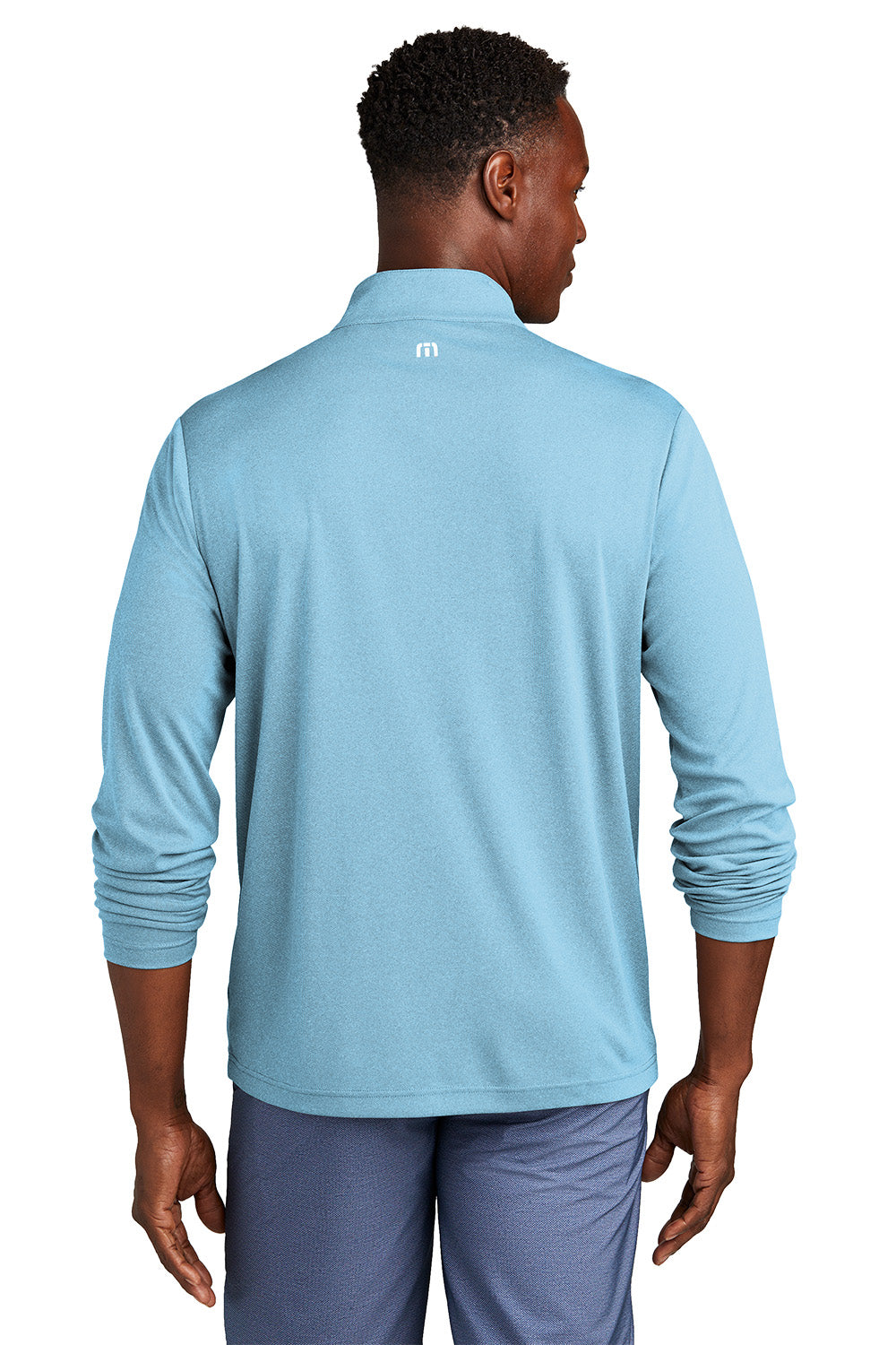 Man wearing a light blue long-sleeve shirt with a logo on the back, standing against a white background. embroidered TravisMathew Coto Performance 1/4-Zip