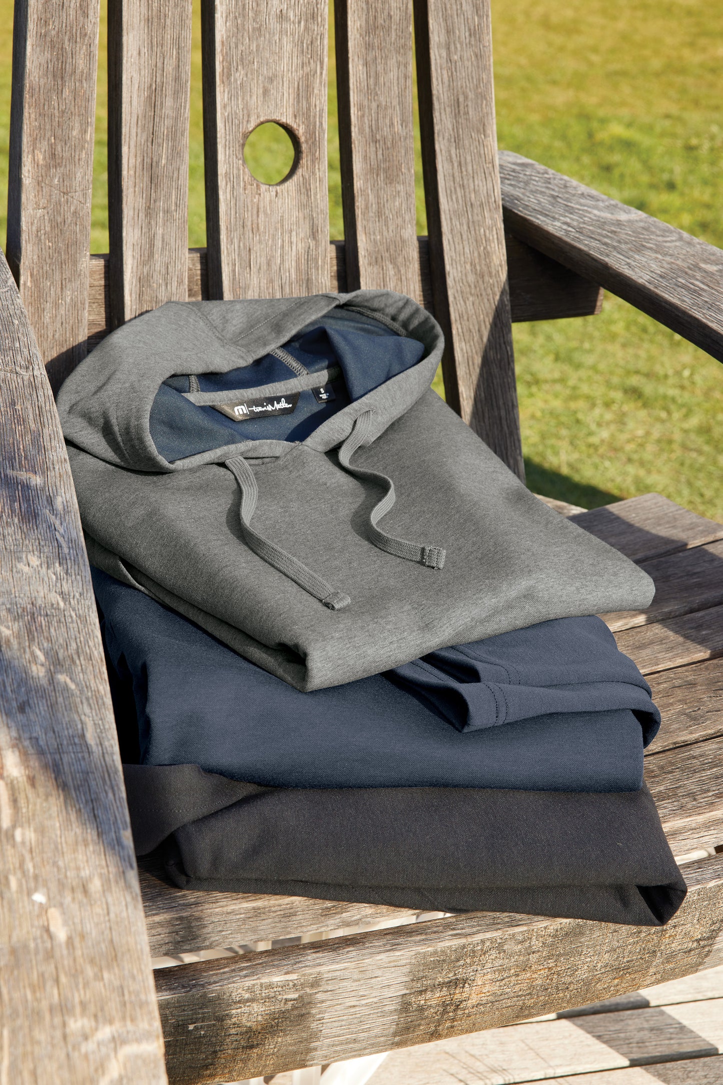 Folded gray and blue clothing on a wooden chair outdoors TravisMathew Coveside Hoodie, Embroidered