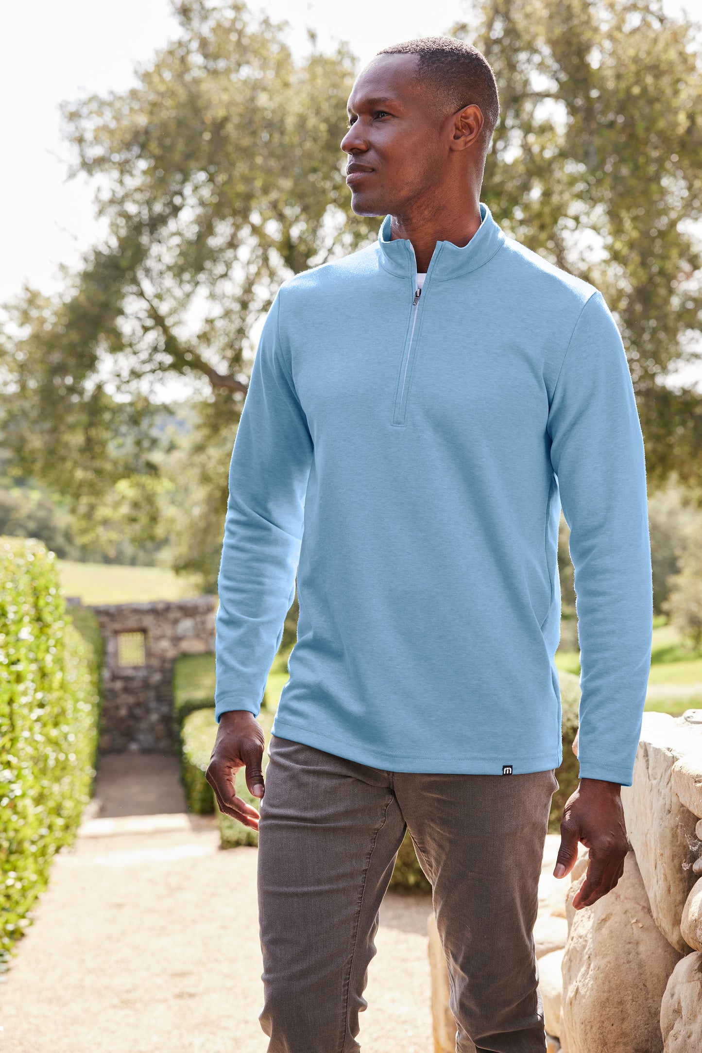 Man wearing a light blue pullover standing outdoors with greenery in the background TravisMathew Coveside 1/4-Zip, Embroidered