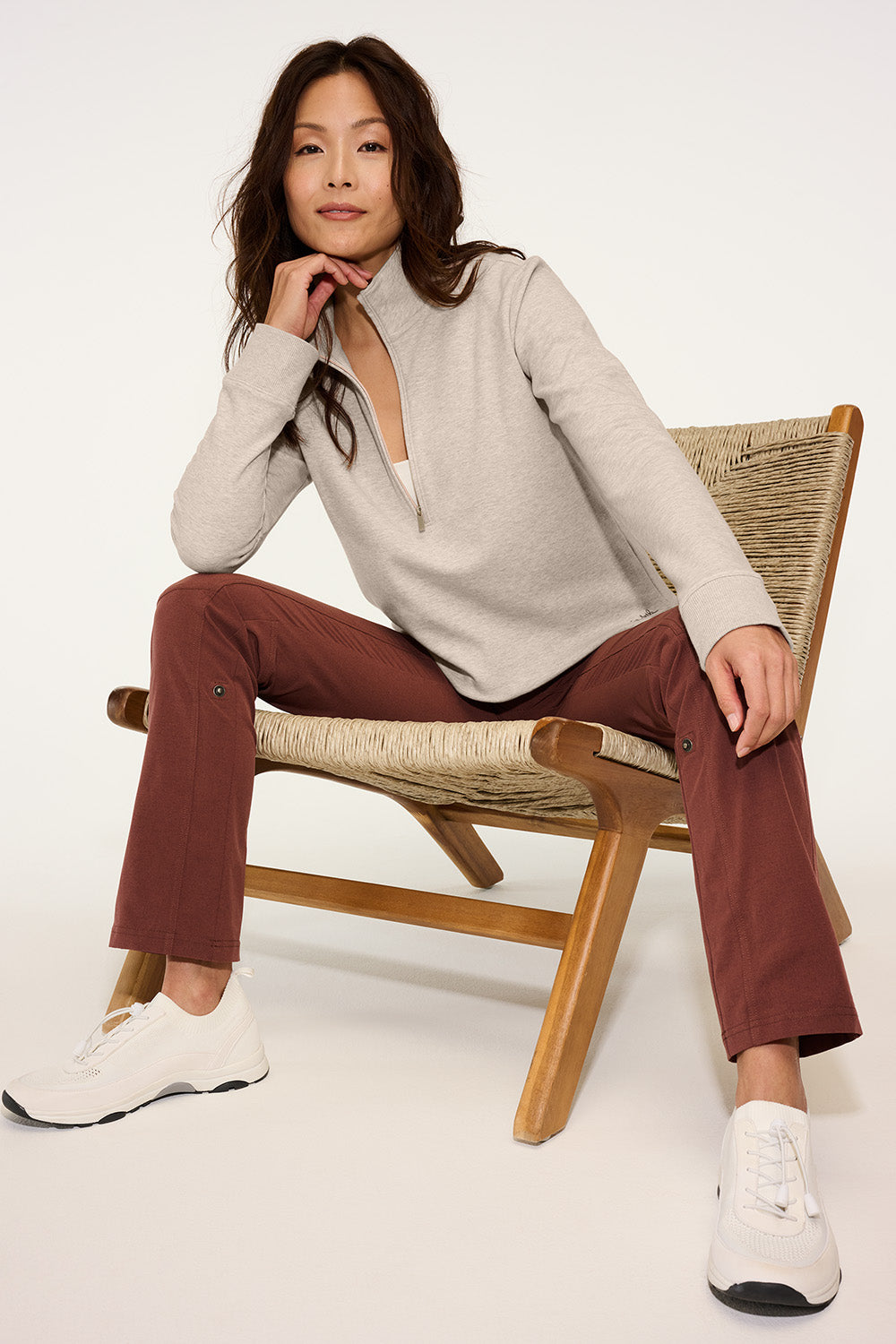 Woman sitting on a chair wearing a beige sweater and brown pants with a white background. TravisMathew Women's Ocean Villa 1/4-Zip, Embroidered