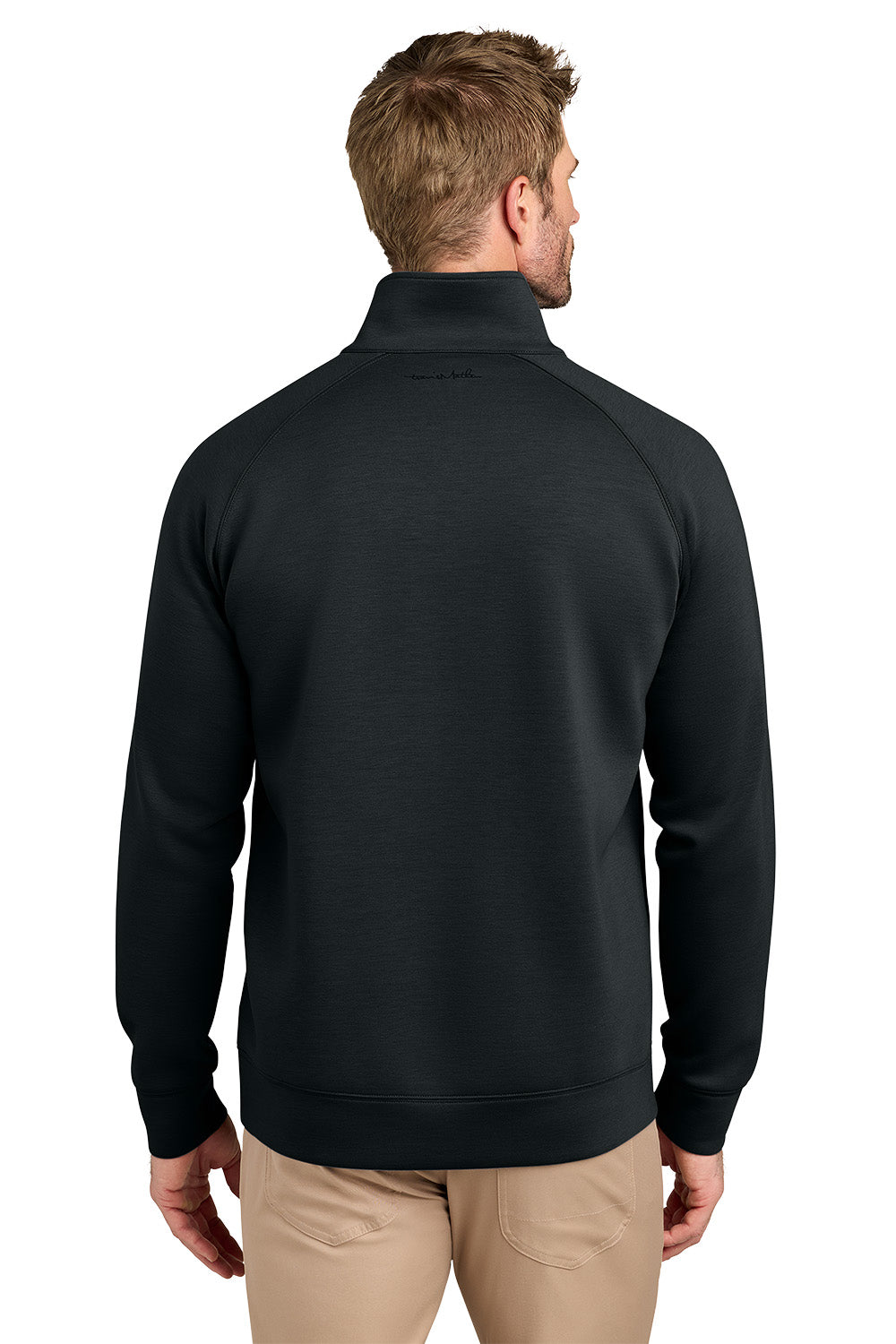 A man viewed from the back wearing a black quarter-zip pullover sweater and khaki pants, set against a plain white background. TravisMathew Momentum Shift 1/4-Zip, Embroidered