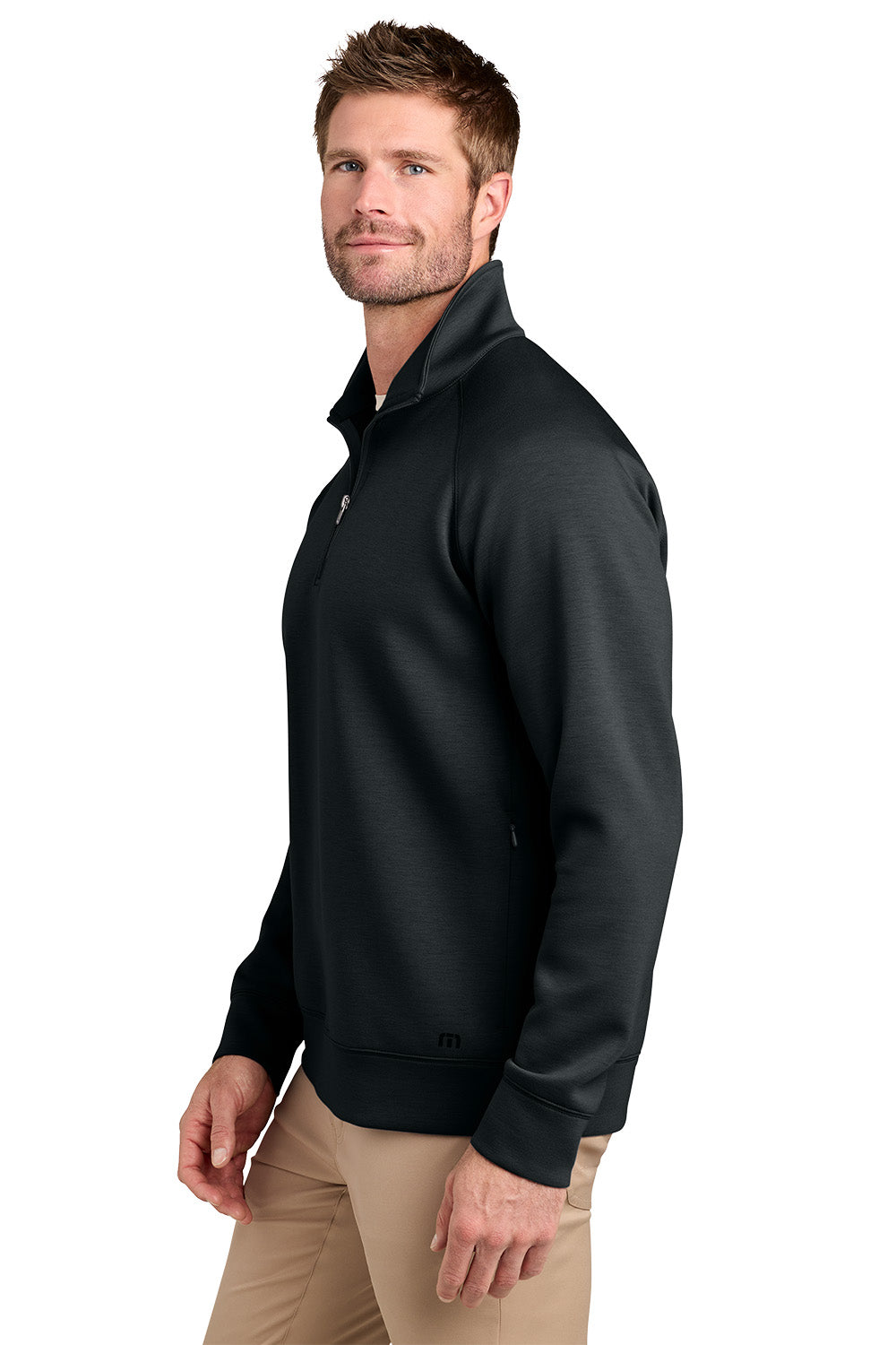 A man wearing a black quarter-zip pullover jacket and khaki pants, shown from a side profile against a plain white background. TravisMathew Momentum Shift 1/4-Zip, Embroidered