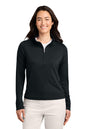 A woman modeling a black long-sleeve quarter-zip pullover with a mock neck, paired with light beige pants, against a plain white background. TravisMathew Women's Coto Performance 1/2-Zip, Embroidered