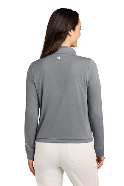A woman shown from the back wearing a heather gray long-sleeve quarter-zip pullover with a small white logo on the upper back, paired with off-white pants, against a plain white background. TravisMathew Women's Coto Performance 1/2-Zip, Embroidered