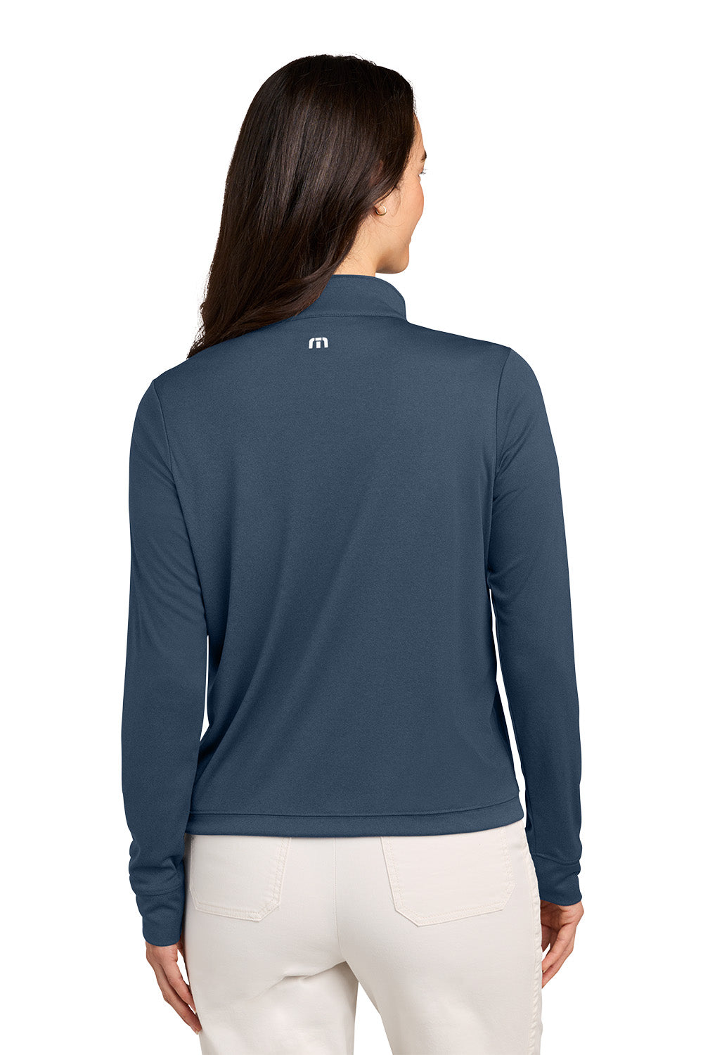 A woman viewed from the back wearing a slate blue long-sleeve quarter-zip pullover with a small white logo on the upper back, paired with off-white pants, against a plain white background. TravisMathew Women's Coto Performance 1/2-Zip, Embroidered