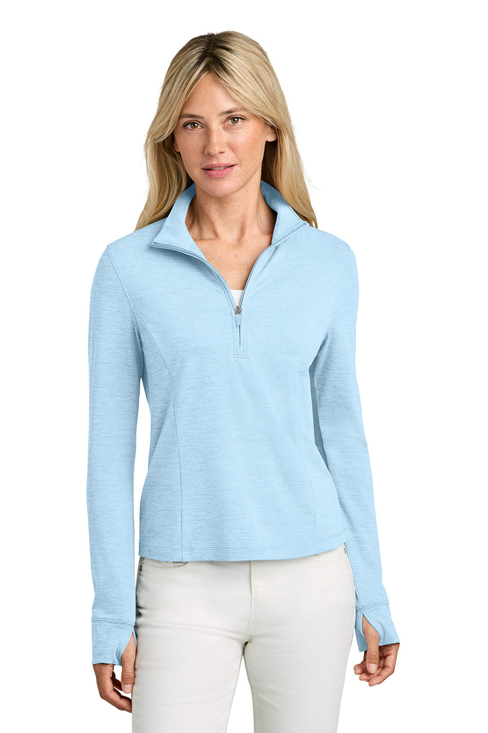 A woman modeling a light blue long-sleeve quarter-zip pullover with a stand collar, paired with white pants, against a solid white background. TravisMathew Women’s Onward 1/2-Zip, Embroidered