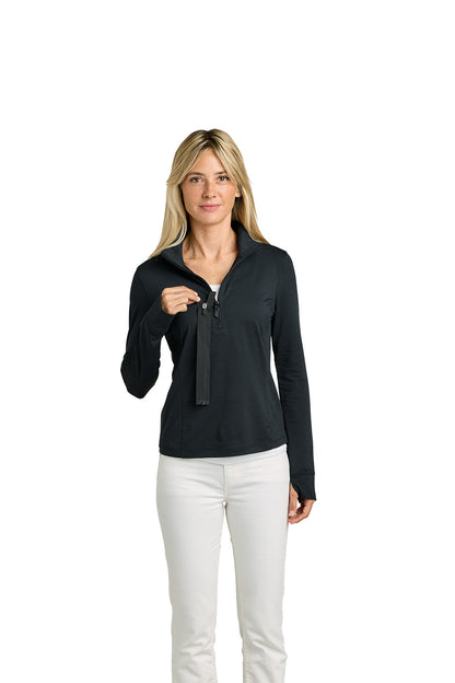 A woman modeling a black long-sleeve half-zip pullover with a split collar, paired with white pants, against a solid white background. TravisMathew Women’s Onward 1/2-Zip, Embroidered