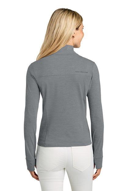 Woman wearing a gray long-sleeve shirt with a brand logo on the back, standing against a white background. TravisMathew Women’s Onward 1/2-Zip, Embroidered