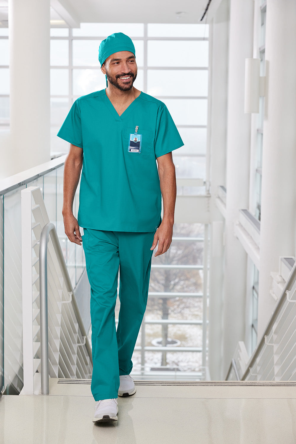 Man in teal medical scrubs walking in a modern building Wink® WorkFlex Scrub Cap, Embroidered