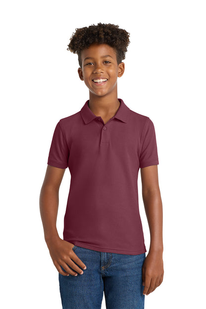Person wearing a maroon polo shirt and blue jeans on a white background. Port Authority® Youth Core Classic Pique Polo, Embroidered by Helmsman Stitch Co.