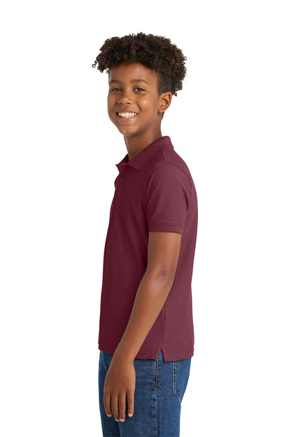 Young boy wearing a maroon polo shirt and blue jeans on a white background. Port Authority® Youth Core Classic Pique Polo, Embroidered by Helmsman Stitch Co.