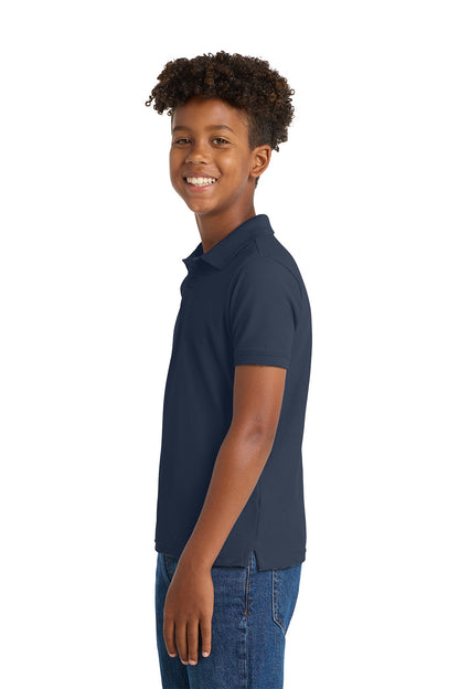 Young person wearing a navy polo shirt and jeans on a white background. Port Authority® Youth Core Classic Pique Polo, Embroidered by Helmsman Stitch Co.