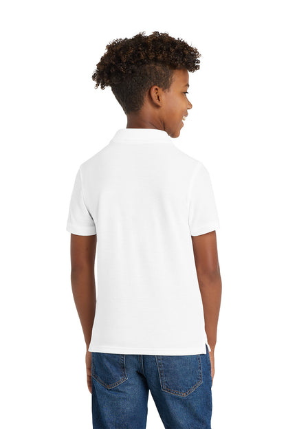 Child wearing a white polo shirt and blue jeans on a white background. Port Authority® Youth Core Classic Pique Polo, Embroidered by Helmsman Stitch Co.
